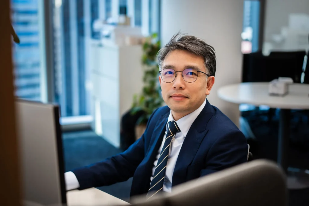 A professional in business-casual attire working at a laptop in a modern office, with retail data visible on the screen.
