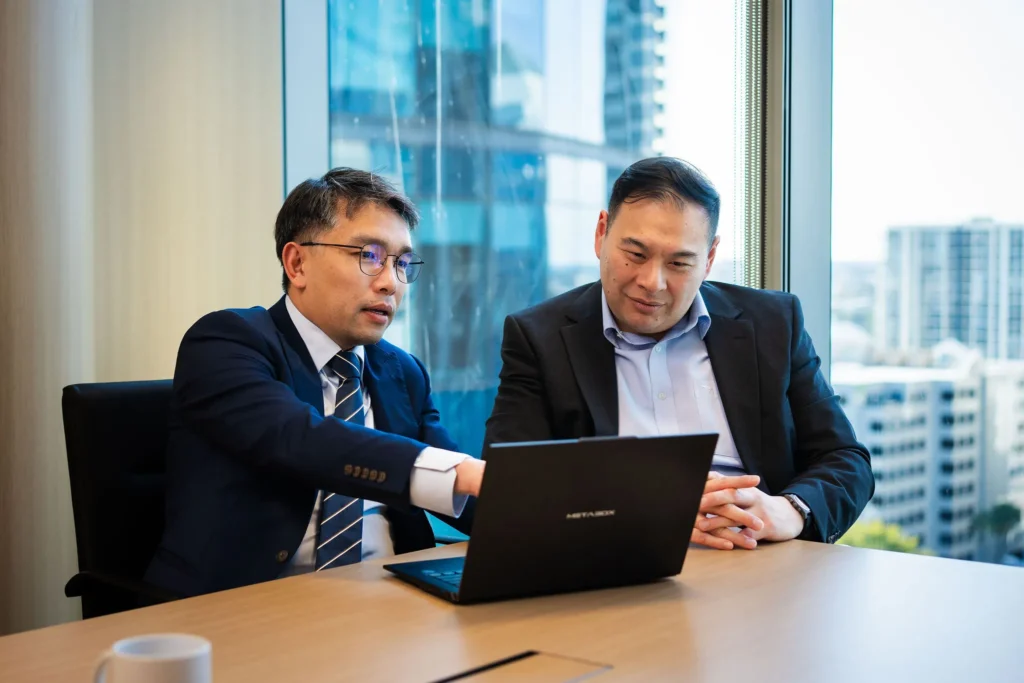 Two Managing Directors in a modern, glass-walled office, leaning in to review a strategic financial dashboard on a sleek laptop.